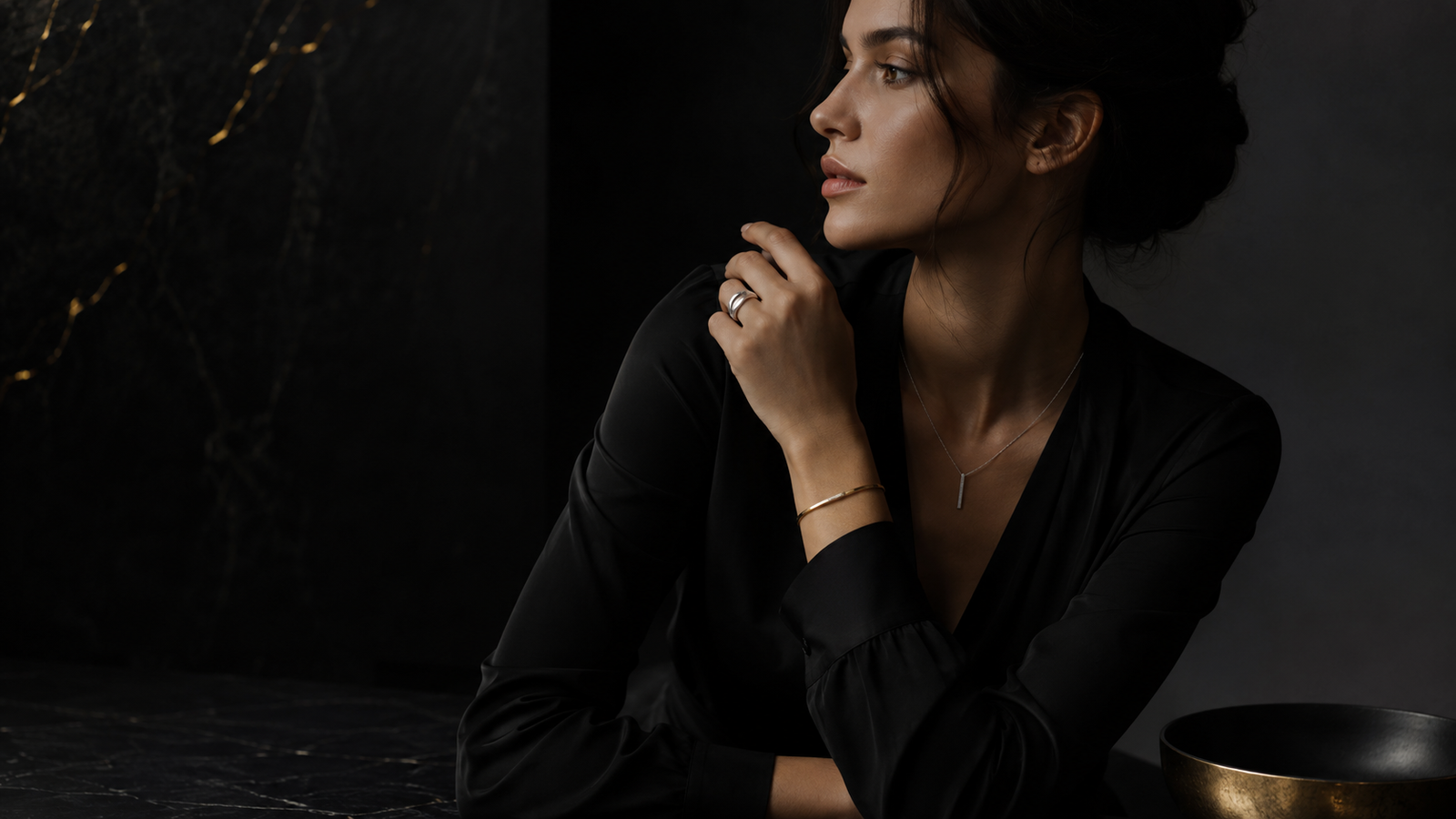 Dark luxury jewelry is not about looking mysterious for the sake of it. It is about restraint, intention, and the quiet confidence of wearing something that does not need to shout. A woman in a dark luxury editorial setting wearing YSNNOIR jewelry with black and gold cinematic lighting.