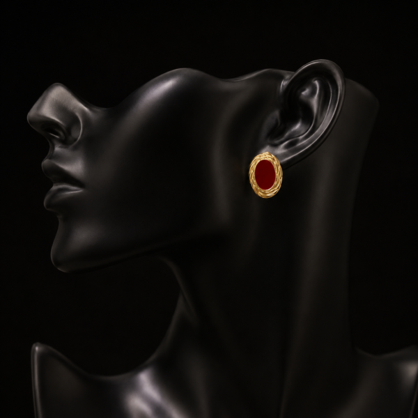 Red oval earring with gold-tone edge on a black mannequin ear