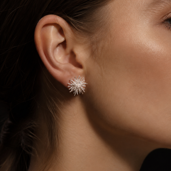 Close-up of a silver-tone starburst stud earring worn on the ear